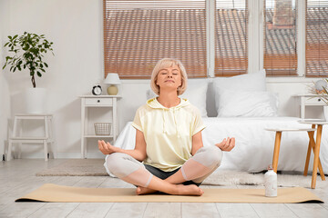 Sporty beautiful mature woman with bottle of water practicing yoga and meditating at home