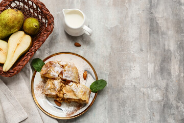 Plate with pieces of tasty pear strudel and fresh fruits basket on grunge grey background