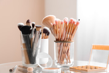 Holders with makeup brushes, palette of eyeshadows and blush on table at home