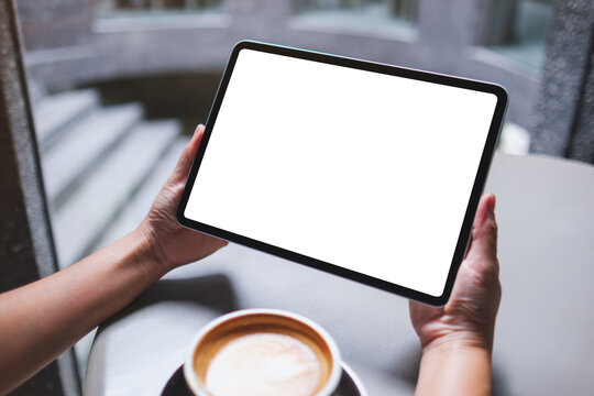 Mockup image of a woman holding digital tablet with blank white desktop screen in cafe