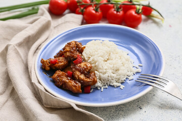 Tasty sweet and sour chicken with rice in plate, napkin and fork on blue grunge background, closeup