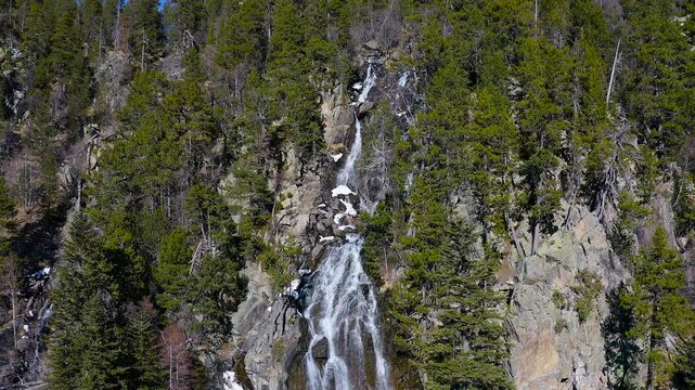 Aerial view of the snowed forest and mountains around a beautiful waterfall La Ratera in the Spanish Pyrenees.