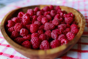 A wooden bowl with ripe raspberries lies on a rustic tablecloth.