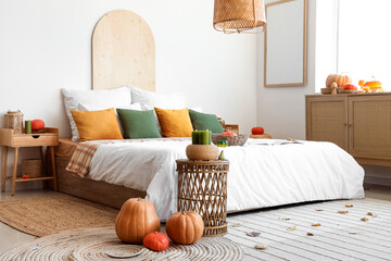Interior of light bedroom with cozy bed, drawers and pumpkins