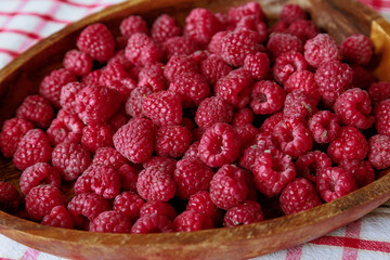 A wooden bowl with ripe raspberries lies on a rustic tablecloth.