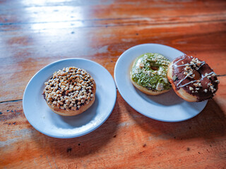 Three donuts served in white plate with various flavor. peanut, chocolate and matcha, side view with brown background