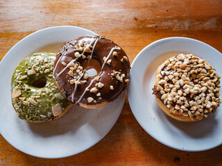 Three donuts served in white plate with various flavor. peanut, chocolate and matcha, top view with brown background