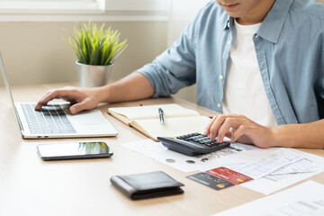 Fototapeta premium Account finance, asian young business man hand using calculator, laptop computer for calculate budget, cost and income of company from paperwork, plan spend money expenses, working on desk at home.