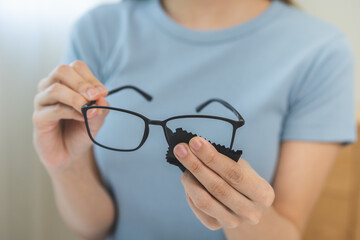 Cleaning glasses concept, close up hand of asian young woman hand holding frame of glass, use cloth wipe the lens, rub to clean eyewear for sanitary with wipe remove dust and disinfect at spectacle.