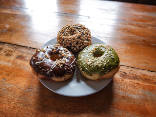 Three donuts served in white plate with various flavor. peanut, chocolate and matcha, side view with brown background