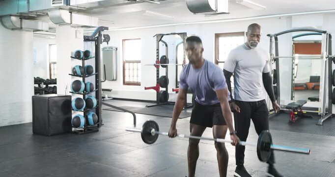 African American male trainee deadlifting after trainer clap receiving guidance on rubber floor