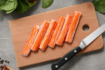 Wooden board with tasty crab sticks and spinach leaves on grey background © Pixel-Shot