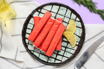 Plate with tasty crab sticks, slices of lemon and dill on lilac background © Pixel-Shot