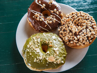 3 Donuts with varios flavour, chocolate, peanut and green tea donuts on the table, green background, top view, served by white plate