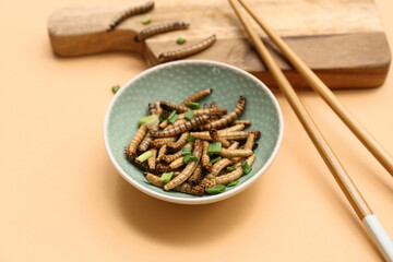 Bowl with fried maggots and green onion on orange background