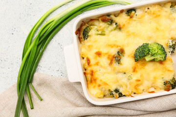 Baking dish with tasty pasta, cheese, broccoli and green onion on light background