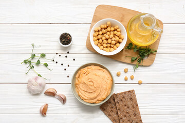 Bowl of tasty hummus with chickpeas, microgreen and crackers on white wooden background