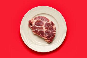 Plate with fresh raw steak on red background