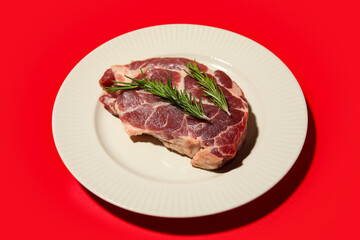 Plate with fresh raw steak and rosemary on red background, closeup