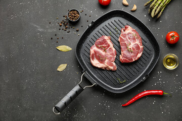 Frying pan with fresh raw steaks and different spices on black background