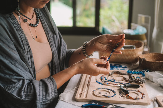 Close up of hands woman jewelry designer. She is sitting at a workspace with tools on it and is creating jewelry by stringing beads on fishing line. The process of creating jewelry. Small business. 