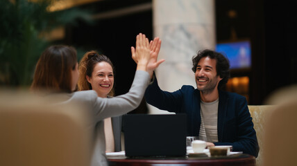 Business team celebrating success with high five, happy colleagues in hotel lobby, teamwork and achievement