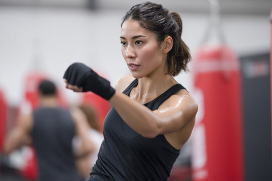 Asian female athlete boxing in gym, focused and determined, wearing black sportswear, punching with intensity