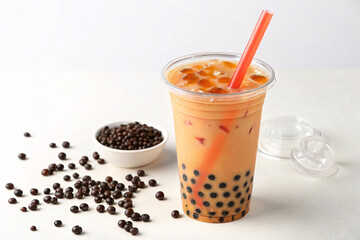 Orange bubble tea with tapioca pearls at bottom, red straw inserted, scattered black pearls and white bowl visible