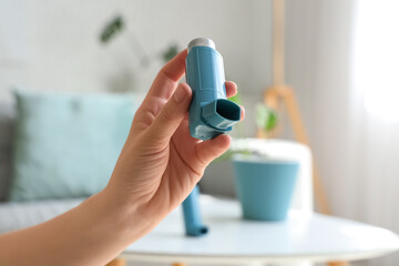 Woman holding modern inhaler in living room, closeup