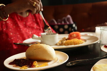 Warm Breakfast Moment with Fresh Bread Roll, Fruit Jam, Omelet, and Coffee – Cozy Dining Table Scene Capturing a Traditional Morning Meal in a Restaurant or Home Kitchen Atmosphere