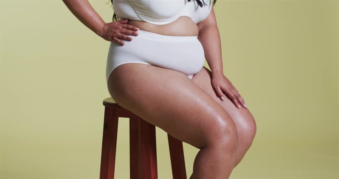 Mid adult woman modeling white lingerie on red stool against yellow backdrop for photoshoot