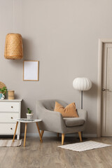 Comfortable armchair with white chest of drawers and floor lamp near grey wall in living room