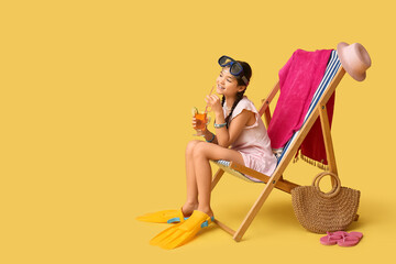 Cute girl in flippers and swimming mask with glass of cocktail sitting in deck chair on yellow background © Pixel-Shot