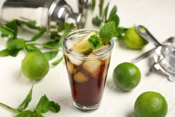 Glass of cold Cuba Libre cocktail with mint and limes on white background, closeup