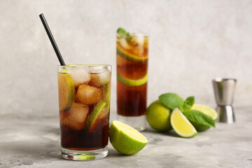Glasses of cold Cuba Libre cocktail with mint and limes on grey background