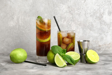 Glasses of cold Cuba Libre cocktail with mint and limes on grey background