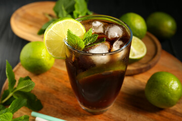 Glass of cold Cuba Libre cocktail with mint and limes on black background, closeup