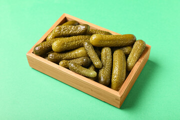 Wooden box with tasty pickled cucumbers on green background, closeup