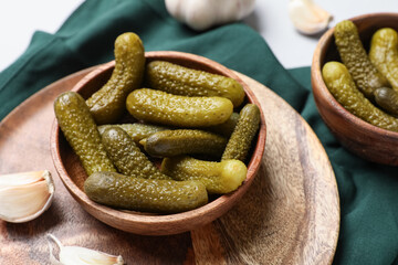 Wooden bowls with tasty pickled cucumbers and garlic on grey background, closeup