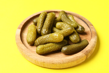 Wooden board with tasty pickled cucumbers on yellow background
