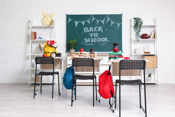 Interior of empty classroom with school desks, shelving units and chalkboard