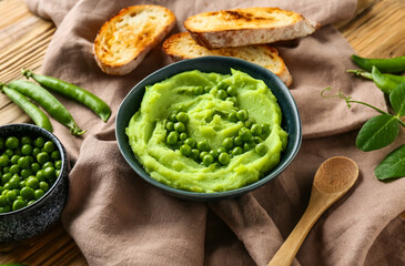 Bowl with mashed green peas and bread slices on wooden background, closeup