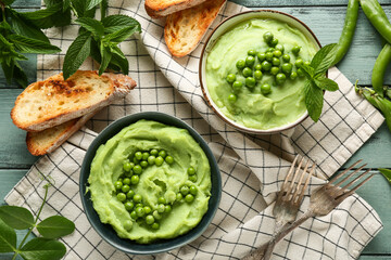 Bowls of mashed green peas with mint and bread slices on blue wooden background