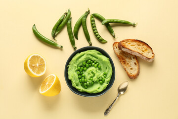 Bowl of mashed green peas with lemon and bread slices on yellow background