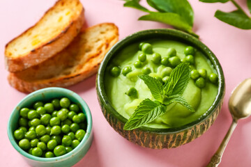 Bowl of mashed green peas with mint and bread slices on pink background, closeup