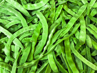 A bunch of green beans are piled on top of each other. They are all green and are in a pile