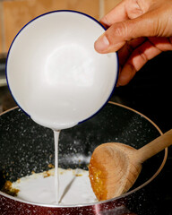 Pouring silky coconut milk into bubbling caramel, Asian fusion cuisine, Diwali festivity, wooden spoon culinary dance