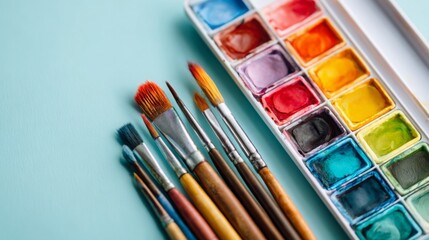Colorful watercolors and paintbrushes arranged on a pastel blue surface in an artist's workspace during a creative session