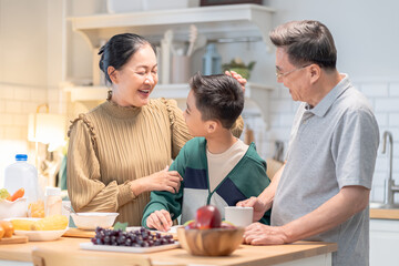 Joyful Asian grandparent, bonding at home lifestyle, warm moment of elderly couple enjoying coffee conversation while grandson stands together, cozy holiday kitchen with relaxed background atmosphere