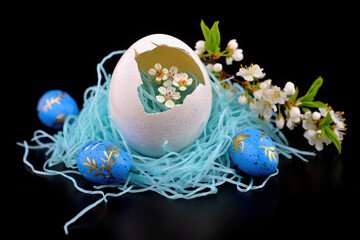 Fototapeta premium Decorated blue and gold easter eggs in a nest with a cracked white egg and spring blossoms
